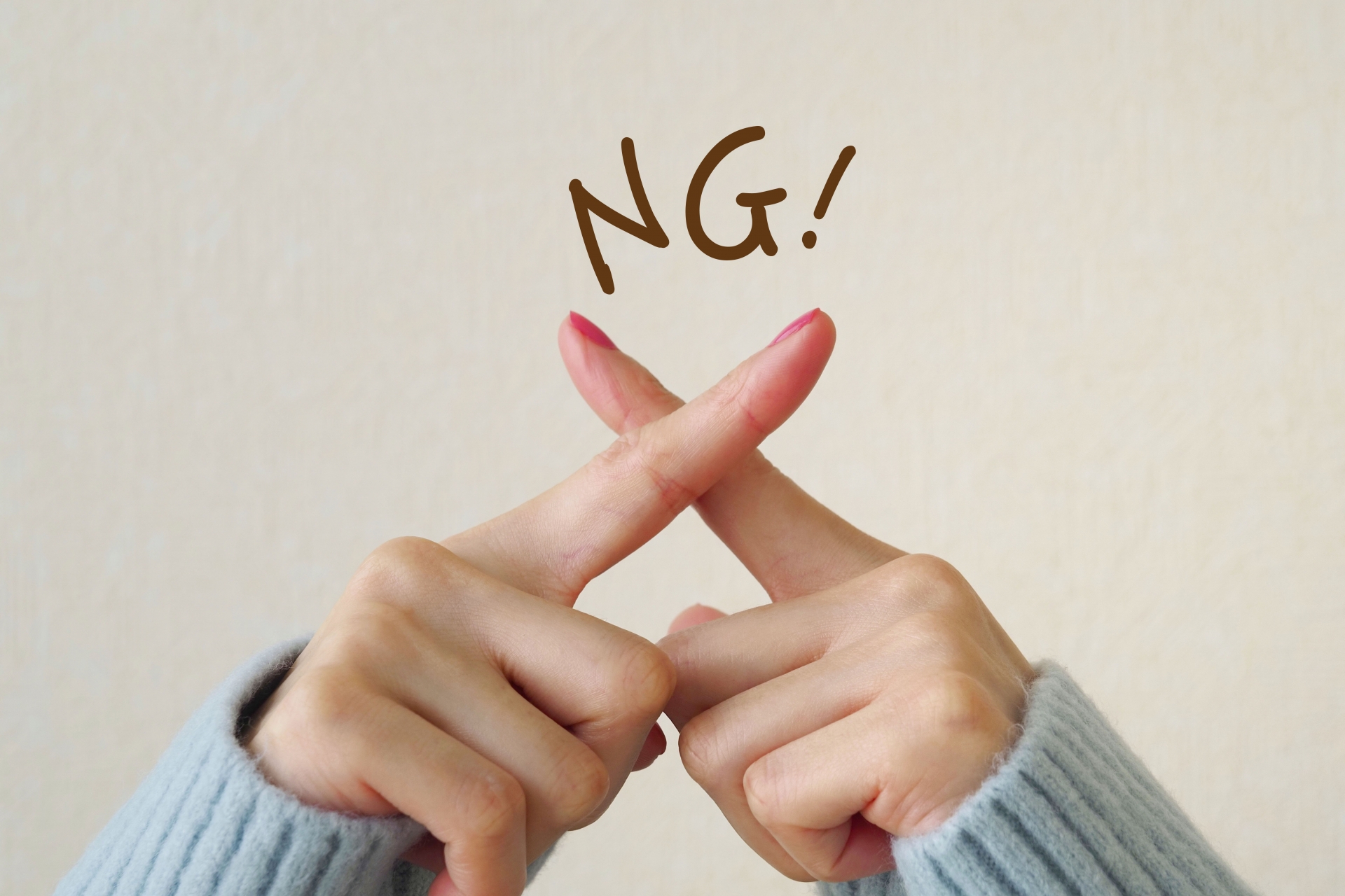 指でバツマークを作る女性の手元